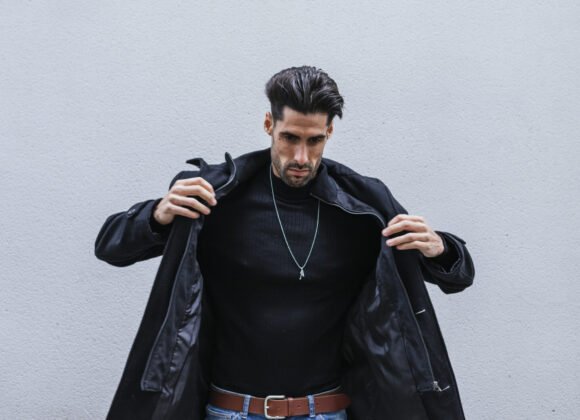 Closeup shot of a stylish man wearing a black coat posing in front of a gray wall