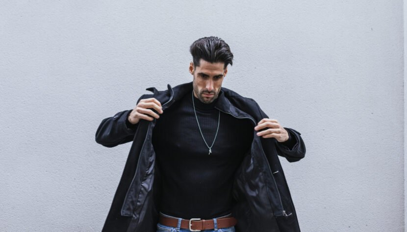 Closeup shot of a stylish man wearing a black coat posing in front of a gray wall