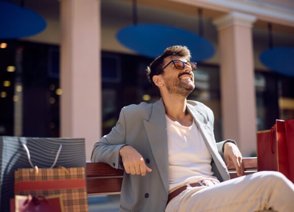 Happy man relaxing on a bench after shopping in the city.