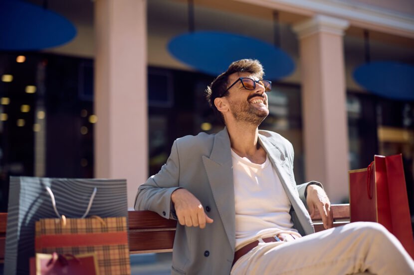 Happy man relaxing on a bench after shopping in the city.
